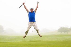 38146792 - excited golfer jumping up and smiling at camera on a foggy day at the golf course