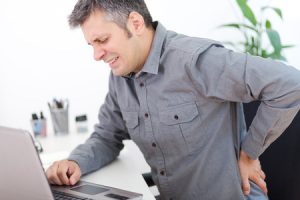 43001190 - image of a young man having a back pain while sitting at the working desk