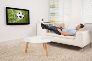 51450368 - relaxed mid adult man lying on sofa while watching football match on television at home