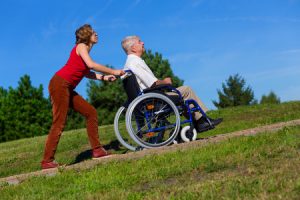 65102715 - young woman push the old man on wheelchair to the top of the hill in the park